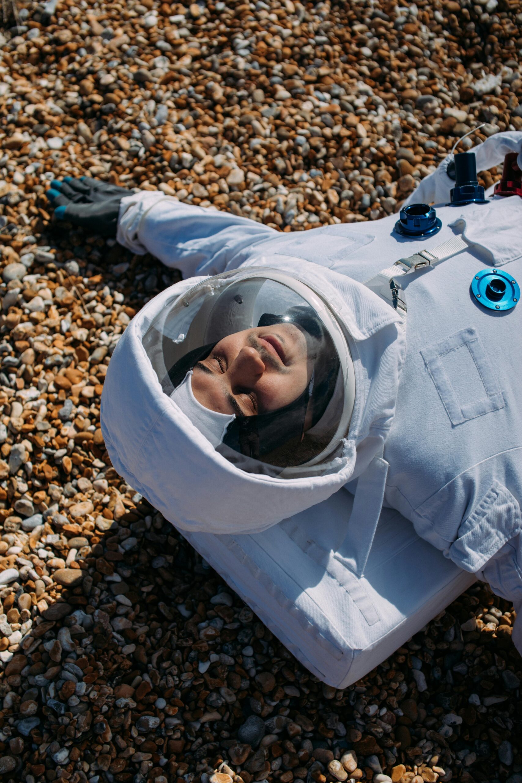 Astronaut in full space suit lays on pebbles enjoying a serene moment outdoors.