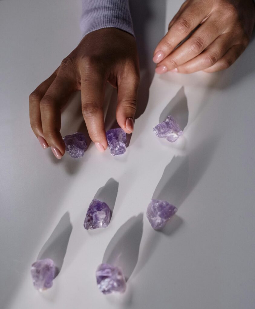 Close-up view of a hand arranging amethyst gemstones on a white surface, highlighting their natural beauty.